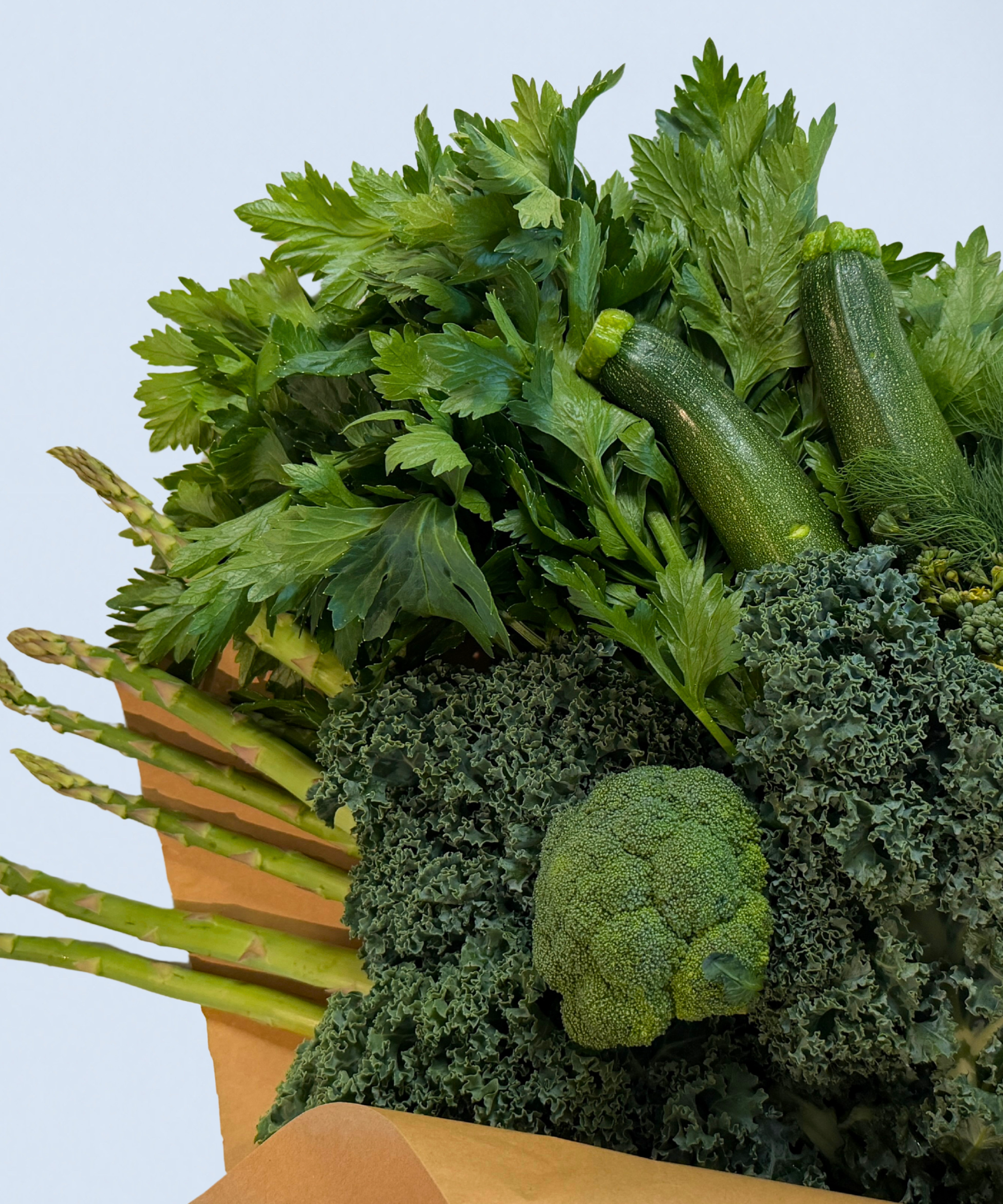 Assorted green vegetables including zucchini, kale, and asparagus on a light blue background