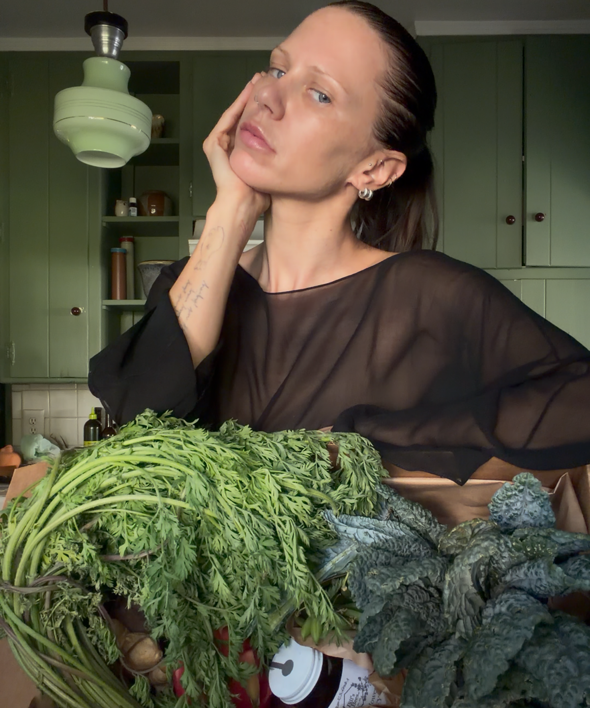 Courtney Trop of @alwaysjudging with her chin in her hand behind carrot greens and dino kale from The Sexy Chef Box by Market Mama, Los Angeles