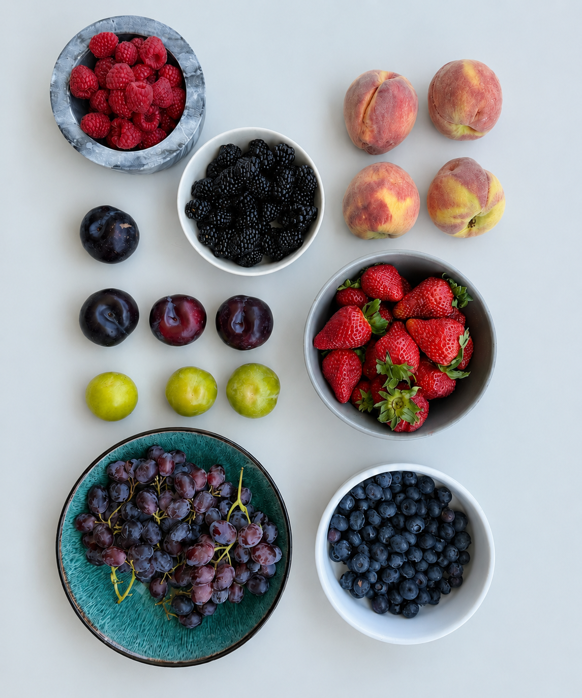 Assorted fruits and berries in bowls on a light background